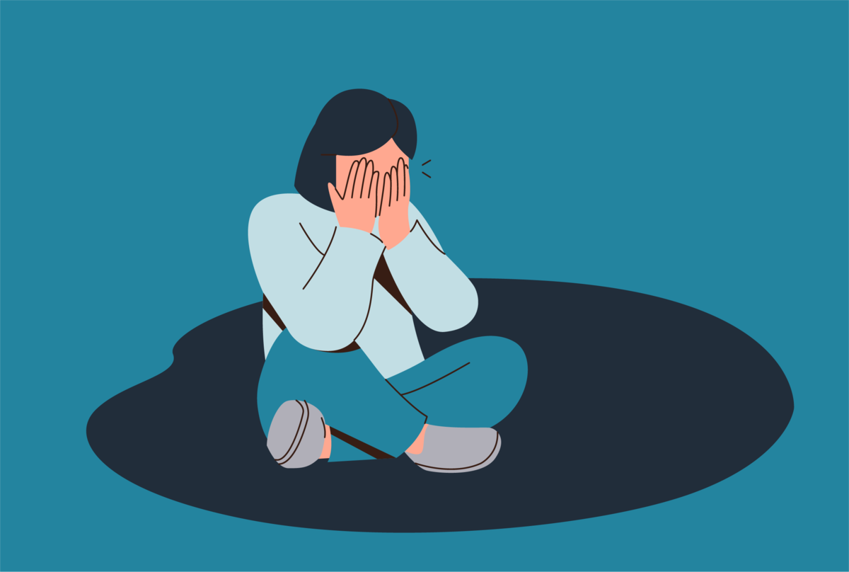 Na obrazku osoba siedząca na podłodze, z zakrytą dłońmi twarzą.